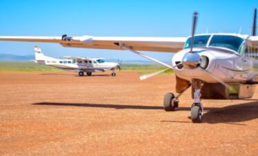 Two white Cessna Caravan safari planes parked on a red dirt airstrip in the Maasai Mara, Kenya, under a clear blue sky
