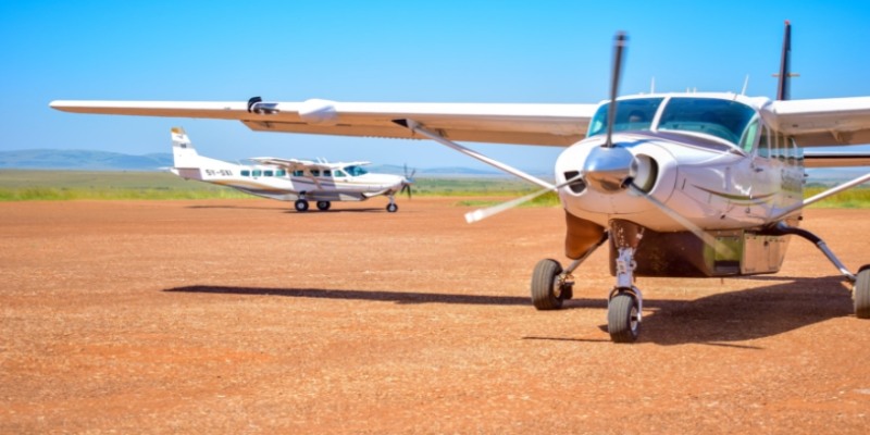 Two white Cessna Caravan safari planes parked on a red dirt airstrip in the Maasai Mara, Kenya, under a clear blue sky