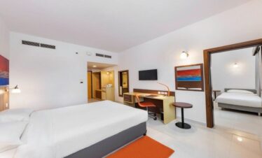 A spacious interconnecting hotel room layout at Citymax Bur Dubai, showing two separate bedrooms joined by an open doorway, featuring white linens and orange decorative accents