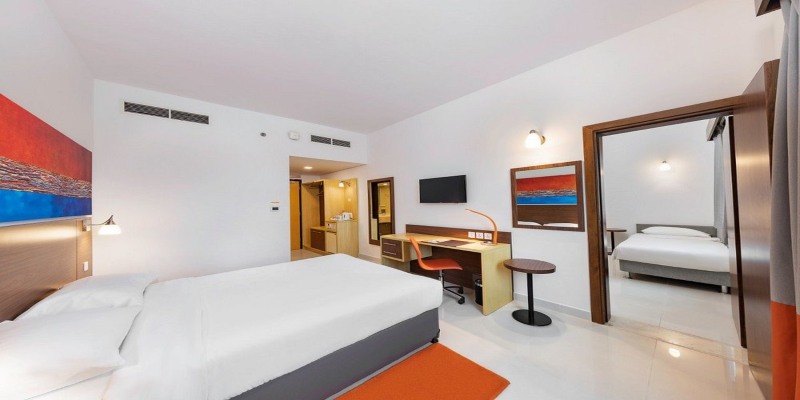 A spacious interconnecting hotel room layout at Citymax Bur Dubai, showing two separate bedrooms joined by an open doorway, featuring white linens and orange decorative accents