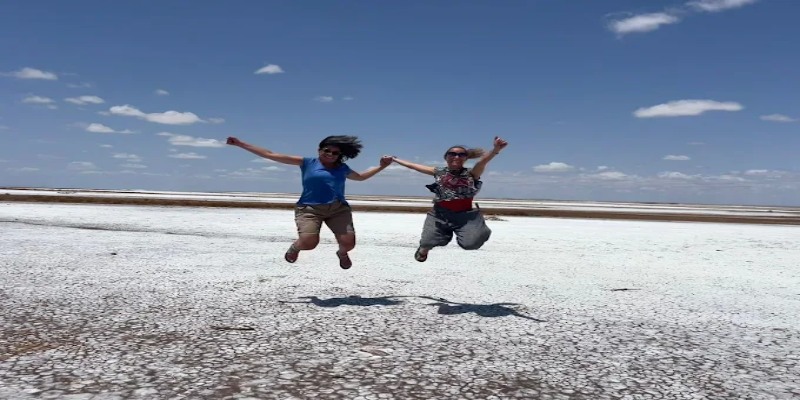 Two female travelers jumping in excitement on the cracked white salt crust during a Chalbi Desert safari in Northern Kenya.