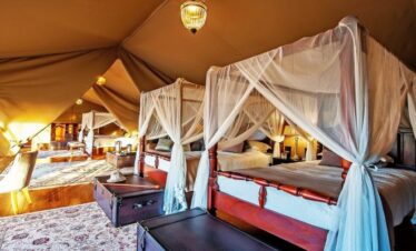 Spacious luxury family tent at Sand River Mara Camp featuring four-poster beds with mosquito netting and elegant safari decor, a premier stay for our 3-Day Kenya Family Safari: Masai Mara & Big Five Adventure
