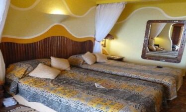 Twin bedroom at Mara Serena Safari Lodge showing two beds with African-print bedding, mosquito nets, and unique wavy wall architecture