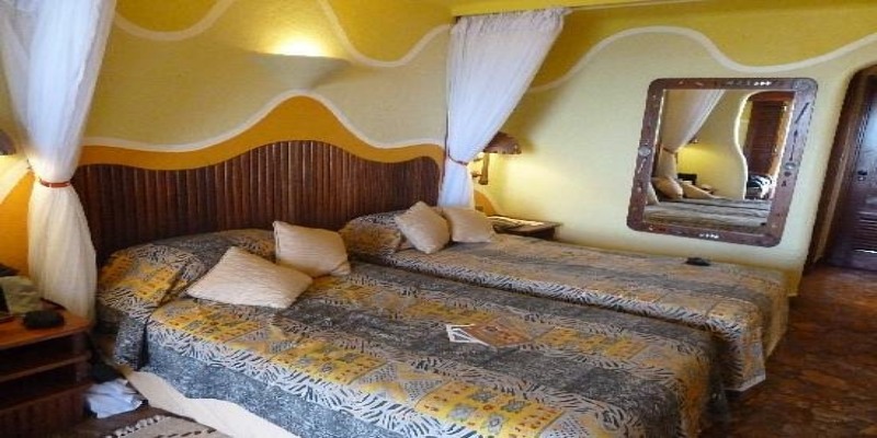 Twin bedroom at Mara Serena Safari Lodge showing two beds with African-print bedding, mosquito nets, and unique wavy wall architecture