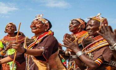 A Samburu warrior teaching a family about traditional beadwork and culture in a village Manyatta
