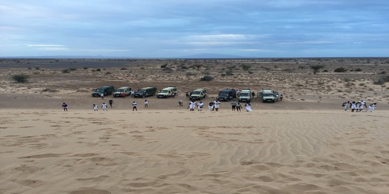A large group of travelers exploring massive sand dunes alongside a fleet of 4x4 vehicles, as detailed in the Chalbi Desert Guide: Kenya’s Stunning White Salt Plain