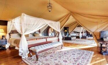 Interior view of a luxury triple-bed family tent at Sand River Mara Camp, featuring elegant four-poster beds and hardwood floors, designed for the 3-Day Kenya Family Safari: Masai Mara & Big Five Adventure
