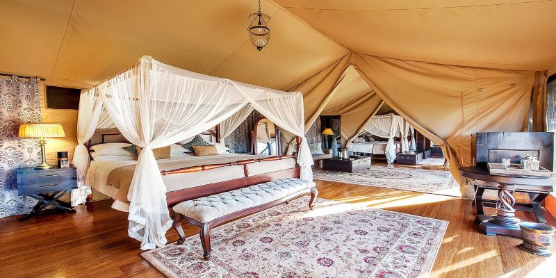 Interior view of a luxury triple-bed family tent at Sand River Mara Camp, featuring elegant four-poster beds and hardwood floors, designed for the 3-Day Kenya Family Safari: Masai Mara & Big Five Adventure