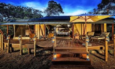 Exterior view of a luxury safari tent at Sand River Mara at dusk, featuring a private wooden deck and lanterns for the 3-Day Kenya Family Safari: Masai Mara & Big Five Adventure