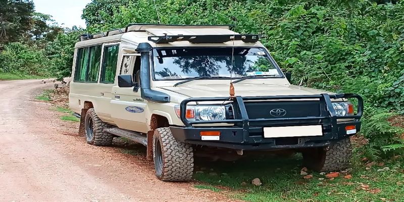 A beige extended 4x4 Land Cruiser safari car parked on a dirt road in Kenya, featuring a pop-up roof for game viewing, snorkel, and reinforced bull bar